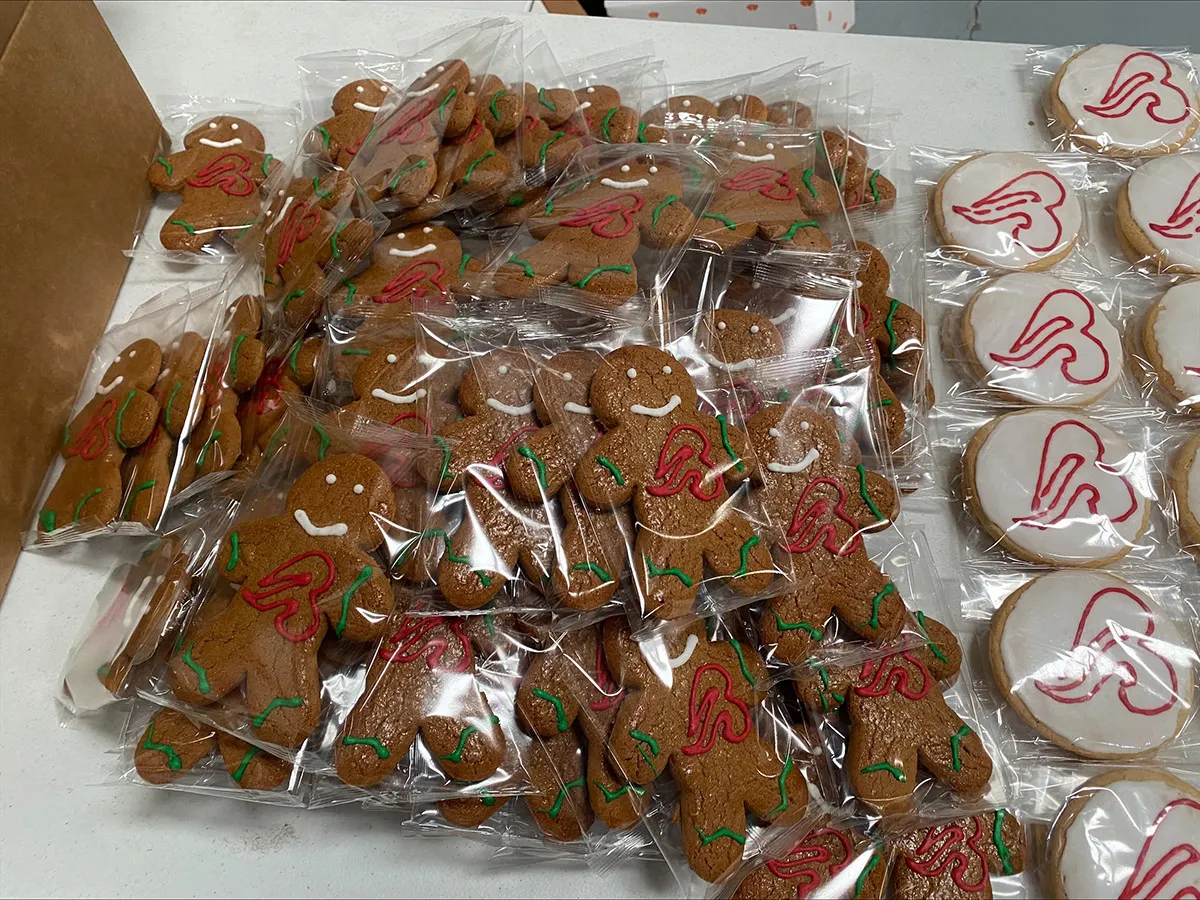 Individually wrapped gingerbread men and iced round sugar cookies with red heart designs on a white table