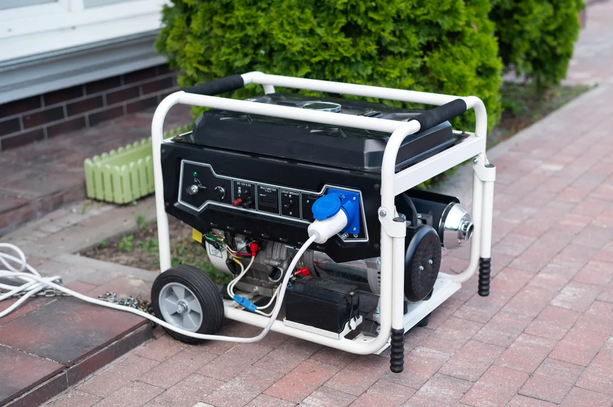 Portable gas generator on driveway with blue outlet plug, wheeled frame for outdoor emergency backup power