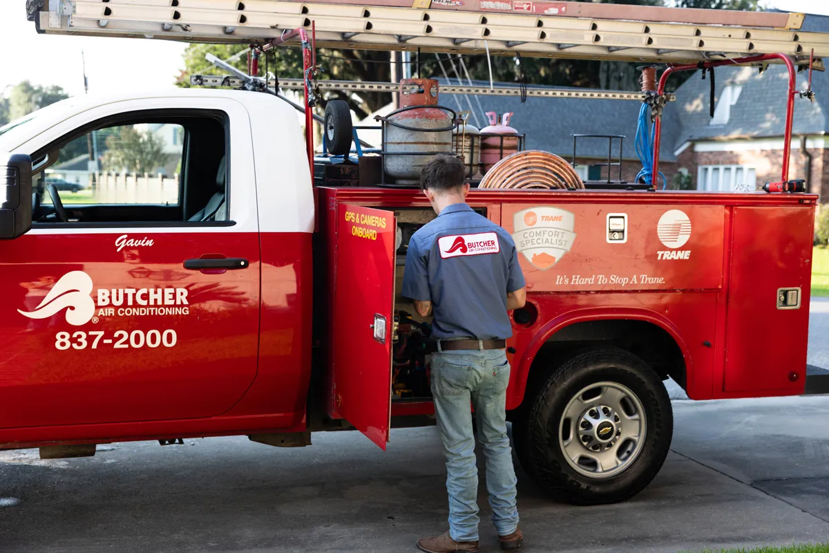 A man, an HVAC technician, at a red Butcher Air Conditioning service truck opening a side compartment