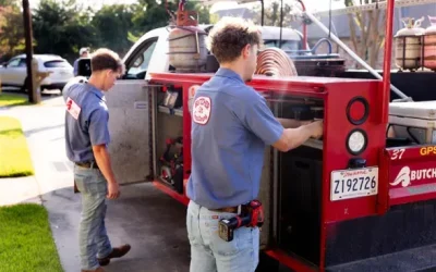 Two technicians in blue shirts accessing equipment compartments on a red service truck in a suburban driveway