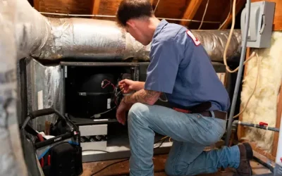 A man kneeling in an attic HVAC unit repairing an air handler, inspecting wiring with toolbox nearby