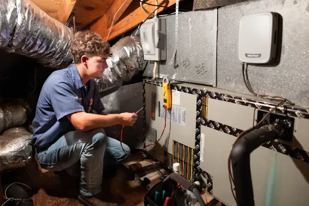 HVAC technician kneeling in attic testing air handler with multimeter near ductwork and control panels