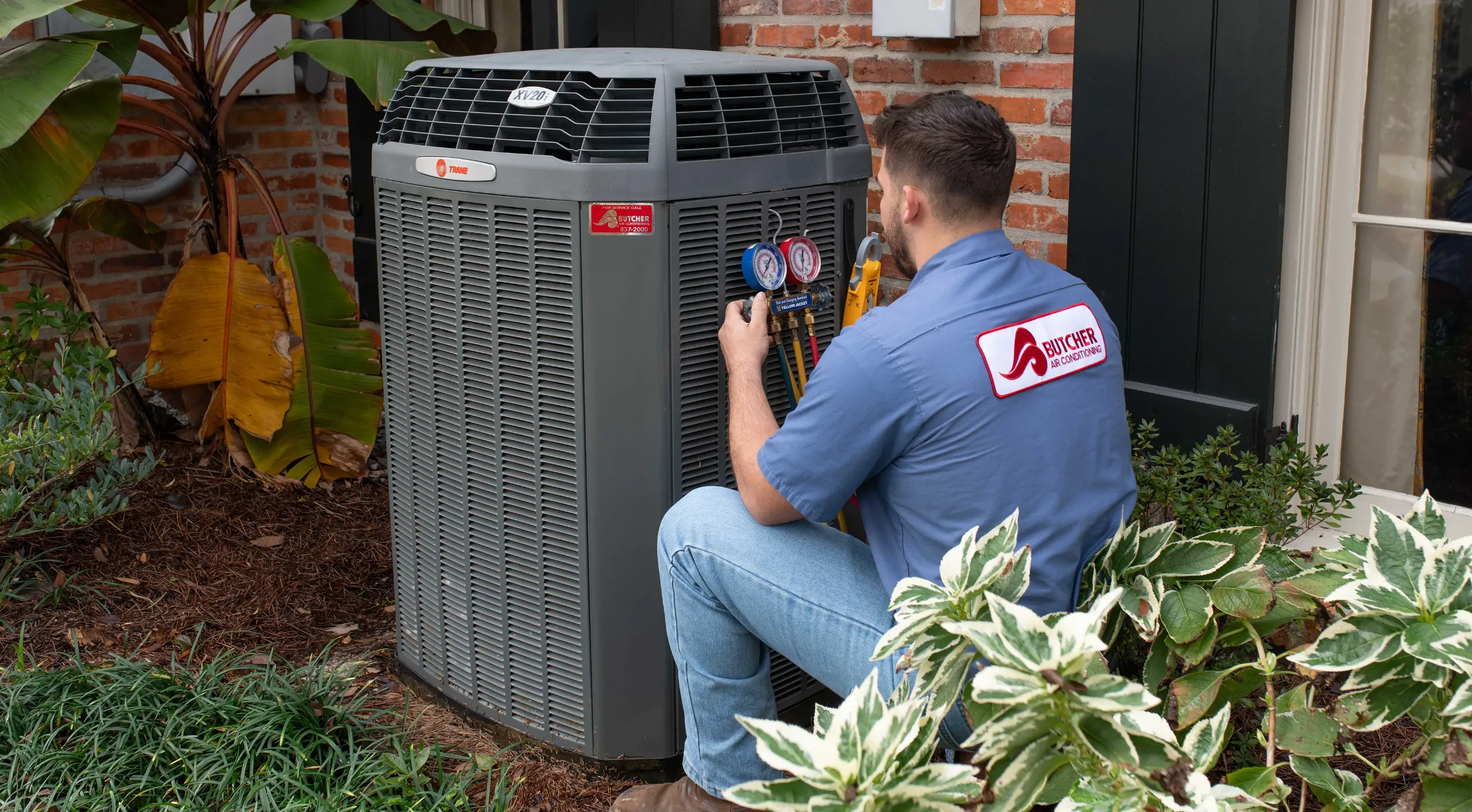 Technician inspecting a Trane outdoor air conditioning unit with pressure gauges, residential HVAC maintenance