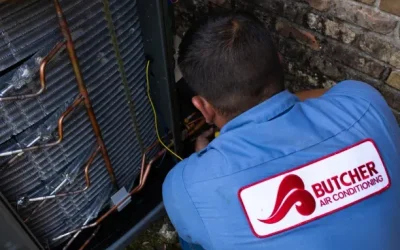 HVAC technician repairing outdoor air conditioner condenser, a man in Butcher Air Conditioning uniform