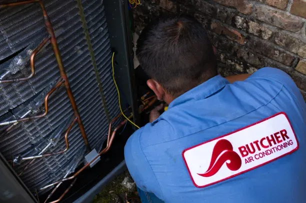 HVAC technician repairing outdoor air conditioner condenser, a man in Butcher Air Conditioning uniform