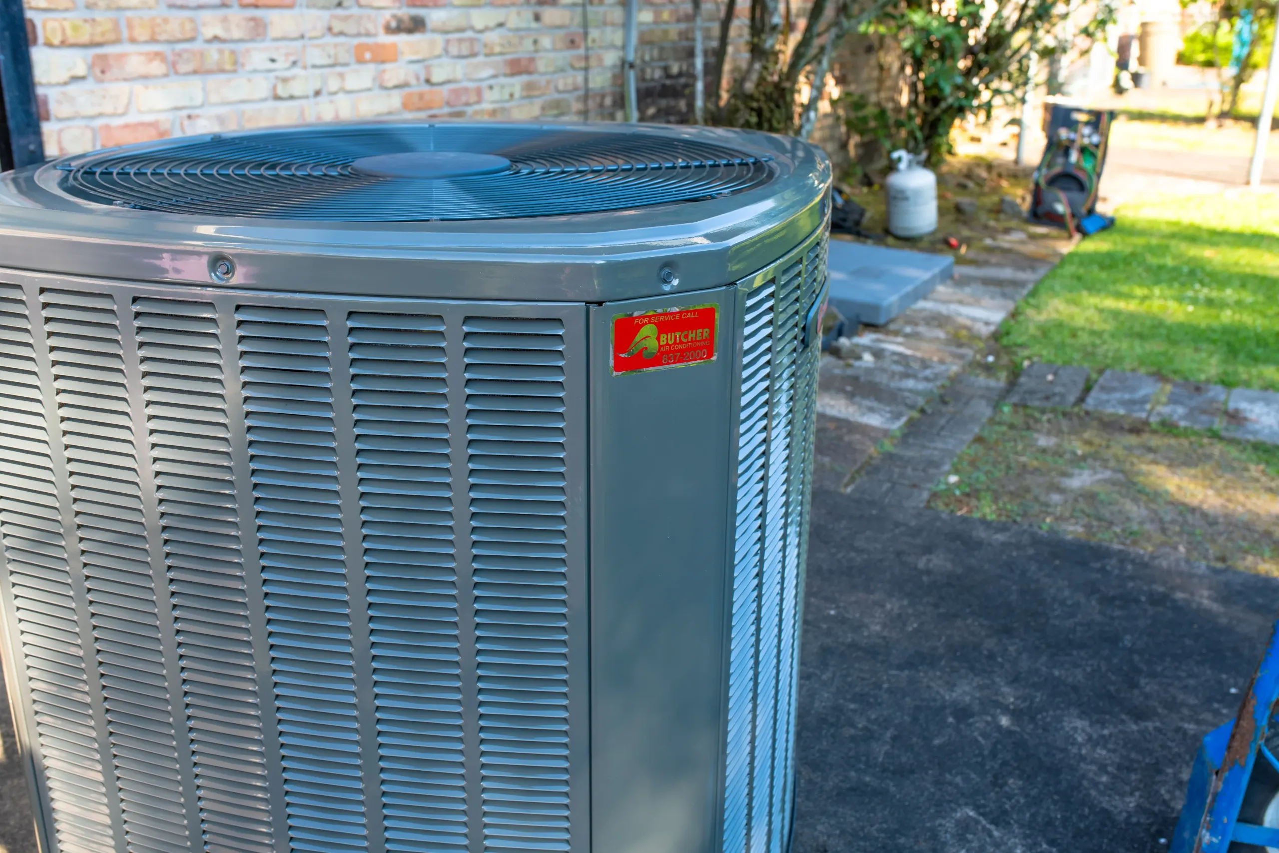 Close-up of outdoor central air conditioner condenser unit beside brick house, gray residential HVAC system