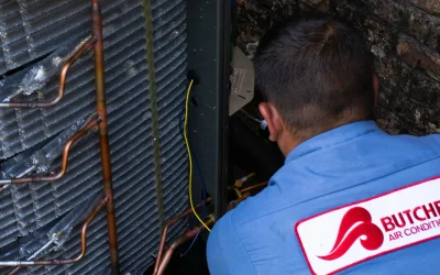 HVAC technician repairing outdoor air conditioner condenser coils and copper tubing beside brick wall