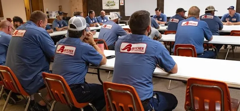 Butcher Air Conditioning technicians in blue uniforms attending team training in a classroom