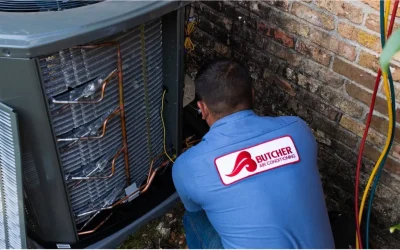 HVAC technician repairing outdoor air conditioning condenser with exposed copper coils and refrigerant hoses by brick wall