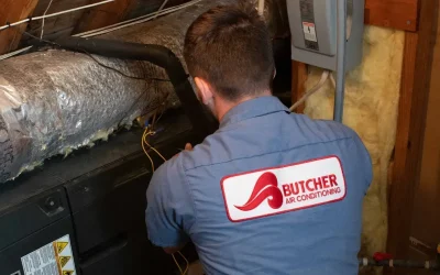 HVAC technician in Butcher Air Conditioning uniform servicing attic air handler and insulated ductwork